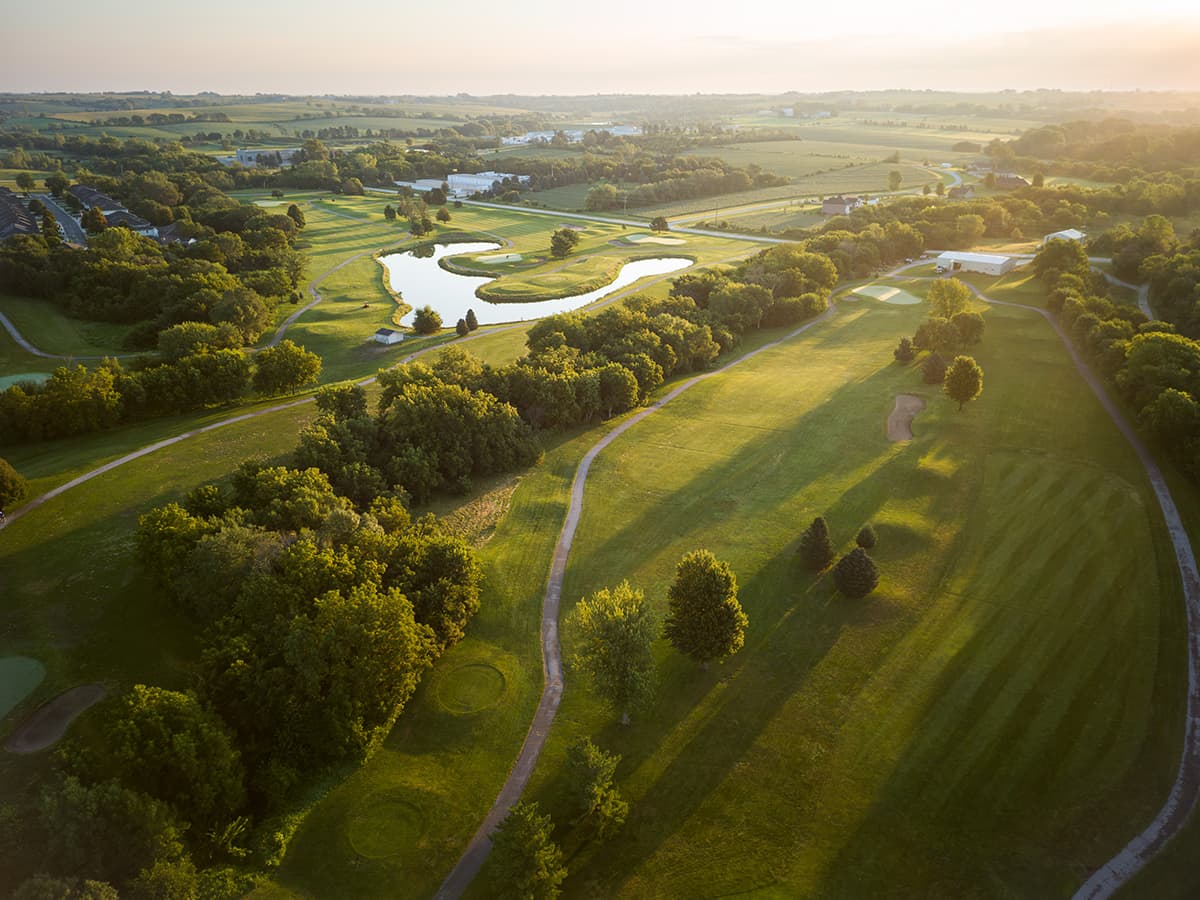 Aerial view of Crooked Creek Golf Club at sunset, featuring lush fairways, winding cart paths, trees, and scenic water hazards.
