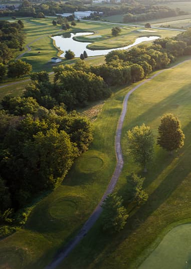 Aerial view of Crooked Creek Golf Club at golden hour, highlighting tree-lined fairways, winding cart paths, water features, and scenic course views.