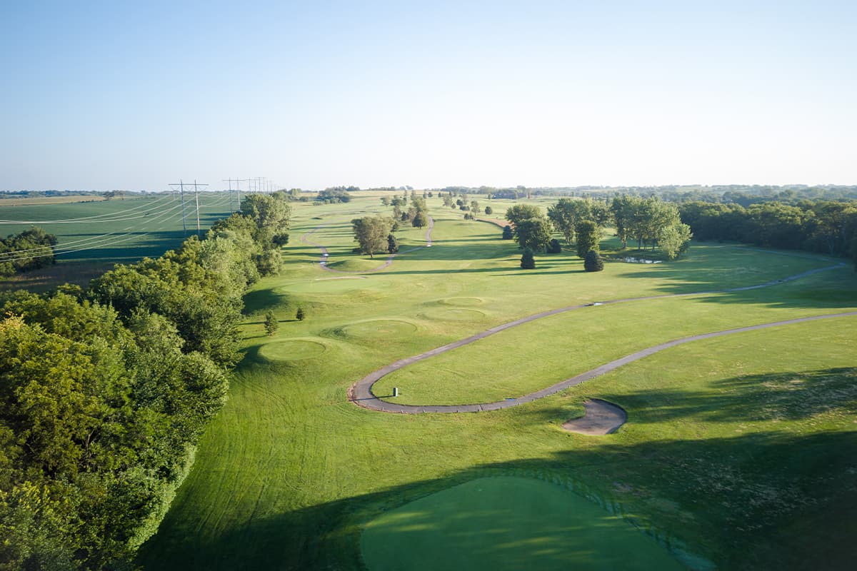 Scenic view of the Crooked Creek Golf Club course featuring rolling fairways, manicured greens, winding cart paths, and mature trees.