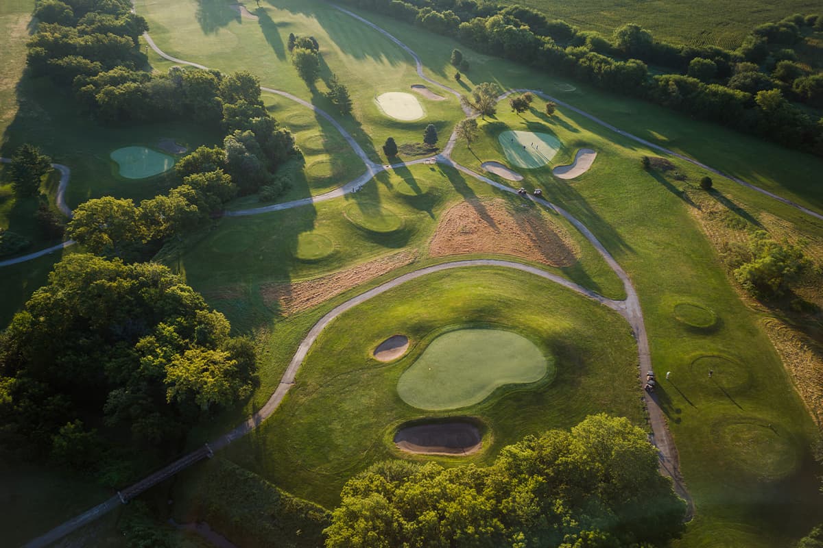 Scenic view of the Crooked Creek Golf Club course featuring rolling fairways, manicured greens, winding cart paths, and mature trees.