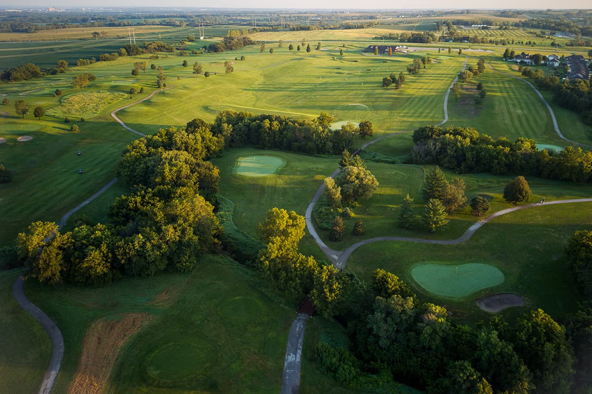 Scenic view of the Crooked Creek Golf Club course featuring rolling fairways, manicured greens, winding cart paths, and mature trees.