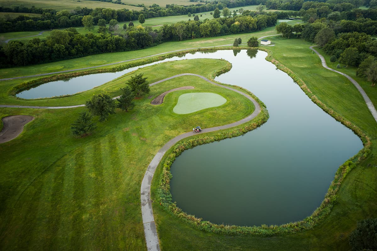 Aerial view of a signature Crooked Creek Golf Club hole featuring a peninsula green, water hazards, winding cart paths, and scenic fairways.
