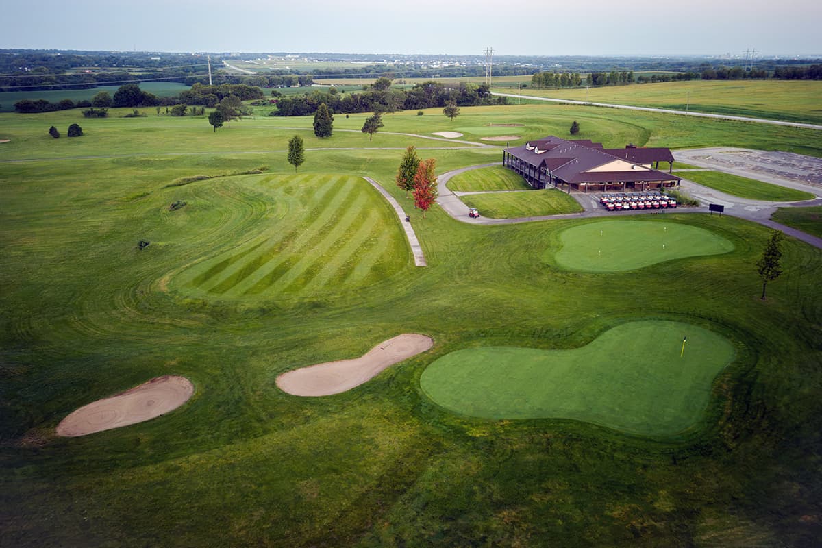 Aerial view of Crooked Creek Golf Club featuring the clubhouse, practice green, manicured fairways, bunkers, and scenic course layout.